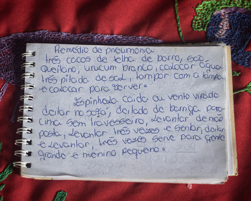 The notebook where Liquinha’s granddaughter has been writing down her prayers and instructions for conducting the healings lays on top of a tablecloth hand embroidered by Liquinha.