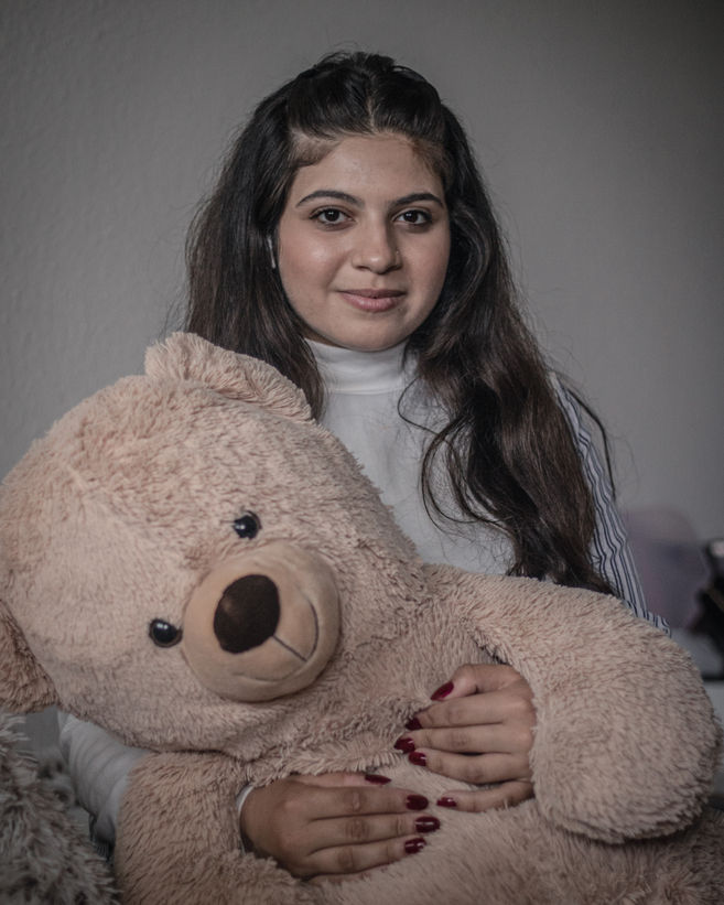 Sara poses for a portrait in her bedroom, holding the teddy bear she got upon her arrival in Denmark, to replace a similar one she had back in Syria.